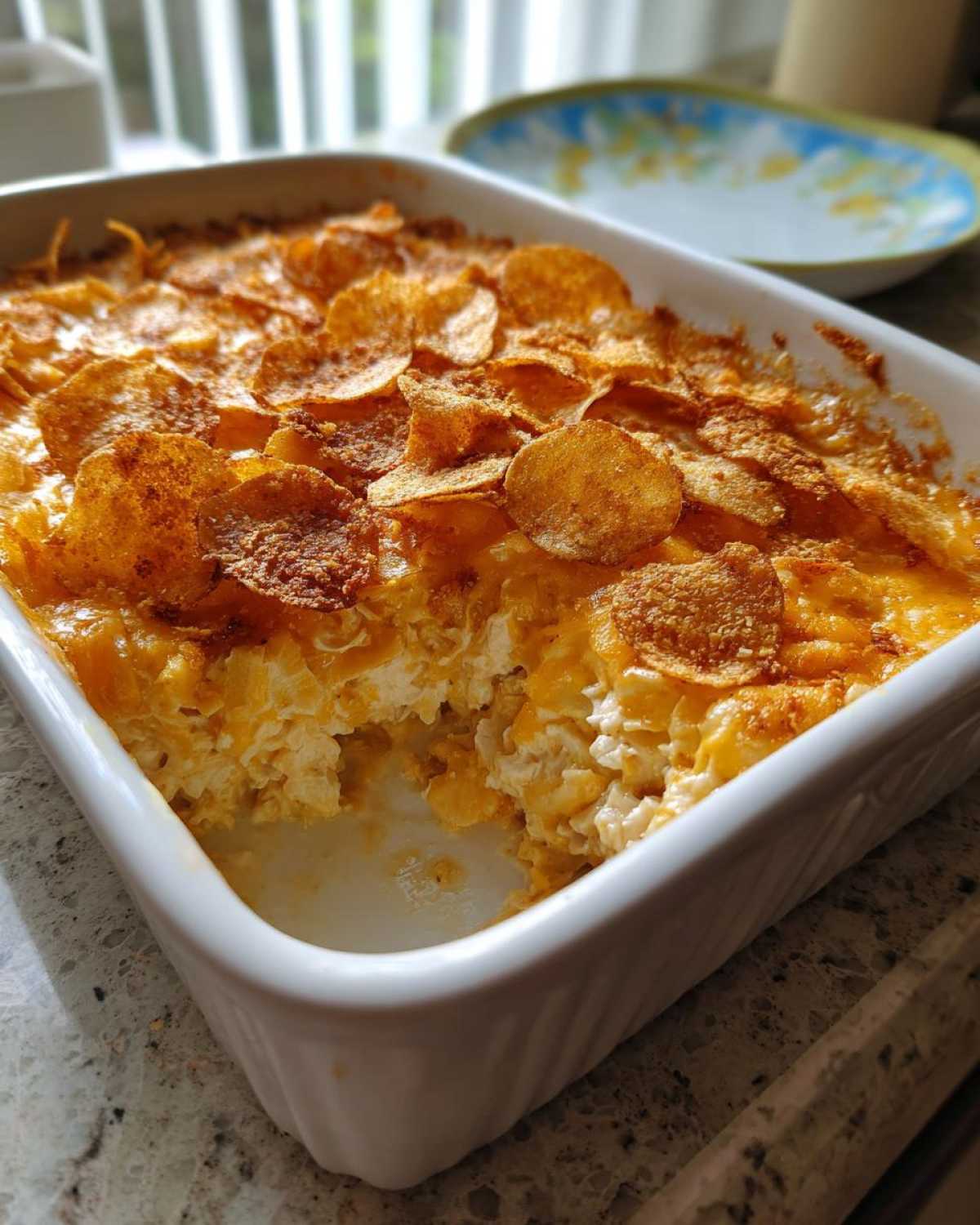 A creamy, cheesy hot chicken salad casserole in a white dish with a golden, crunchy potato chip topping.