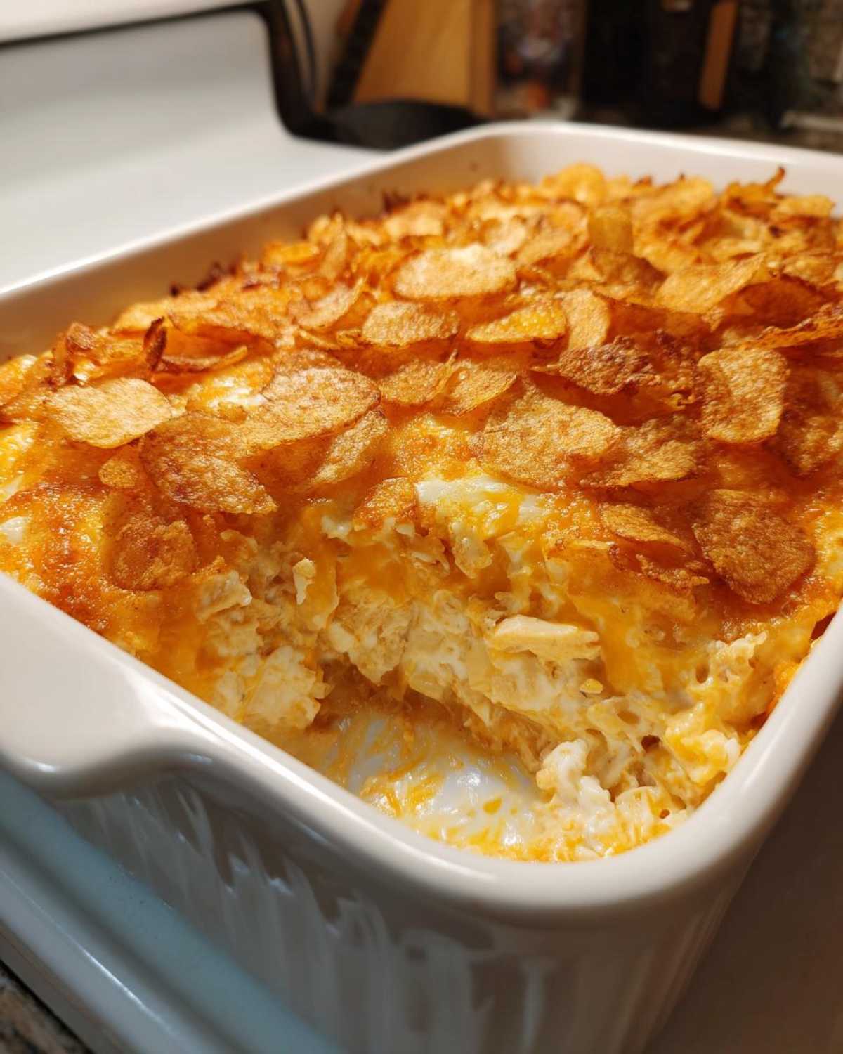 Close-up of a creamy, cheesy hot chicken salad casserole topped with crispy potato chips in a white baking dish.