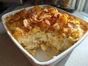 A creamy baked casserole, likely hot chicken salad, topped with golden, crispy potato chips in a white baking dish.