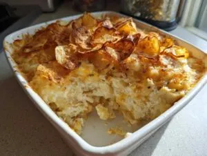 A creamy baked casserole, likely hot chicken salad, topped with golden, crispy potato chips in a white baking dish.