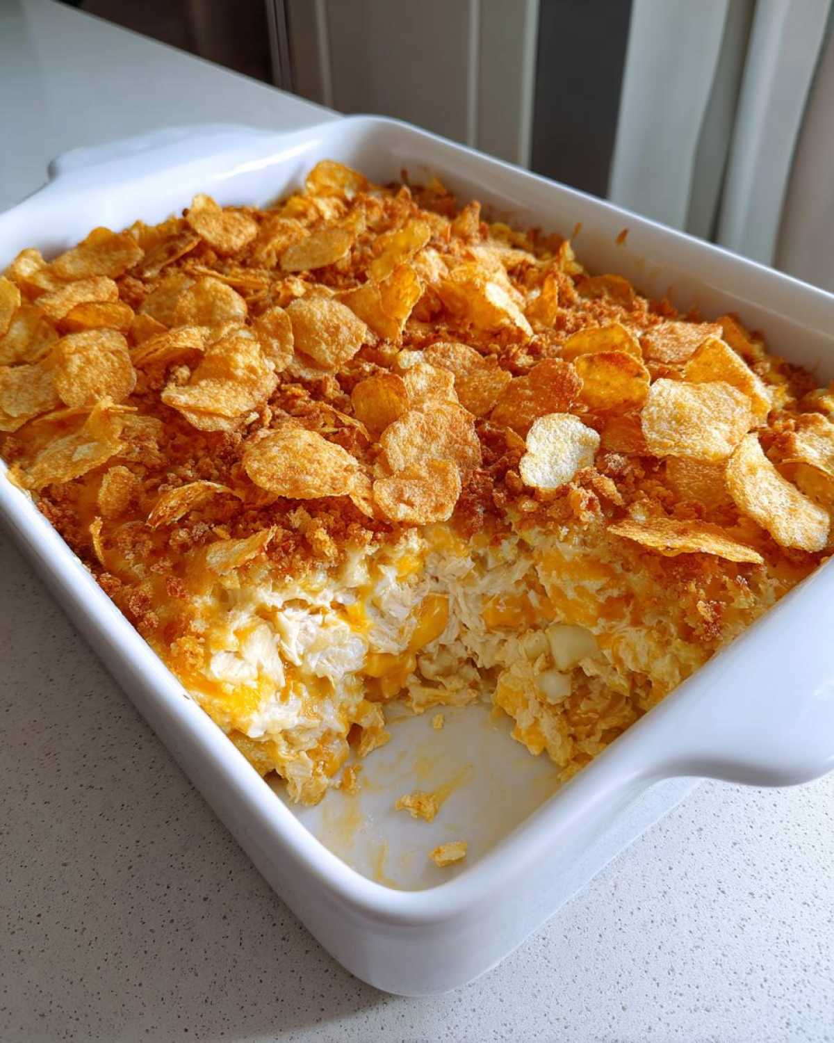 A white baking dish filled with creamy hot chicken salad topped generously with golden, crunchy corn flakes.