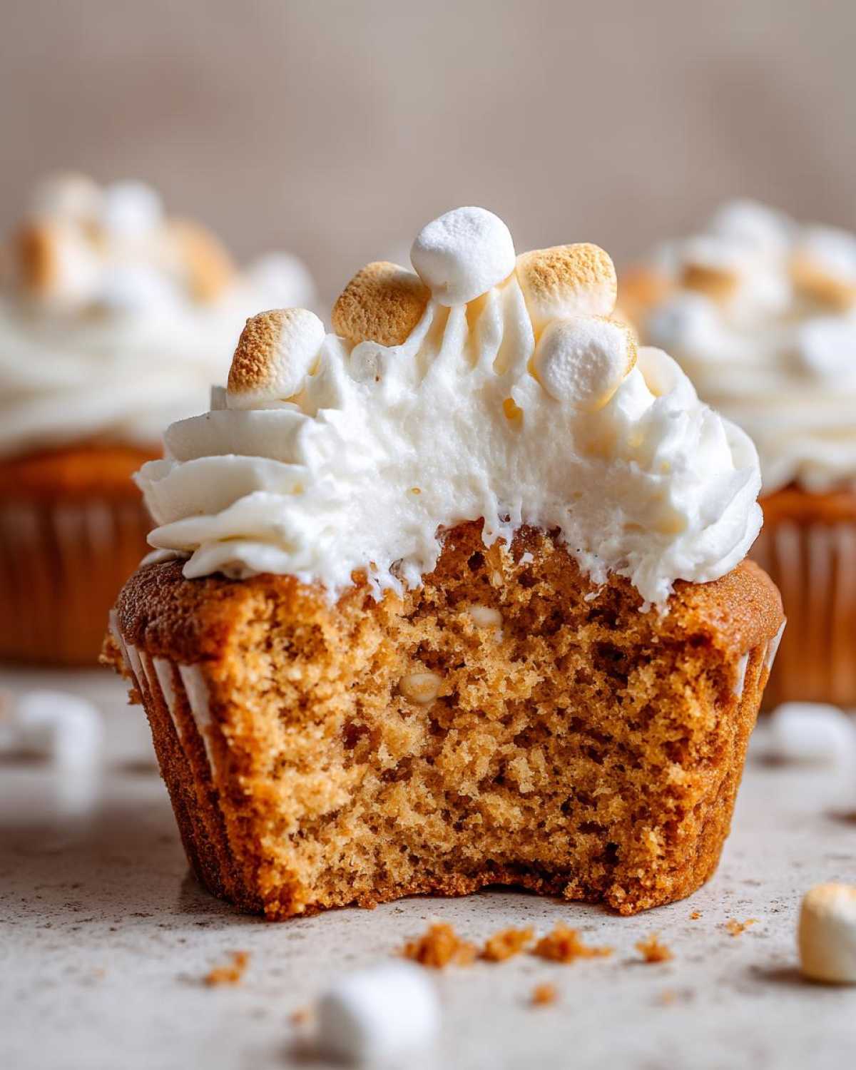 A close-up of a hot chocolate cupcake with a bite taken out, showing the moist interior and marshmallow frosting.