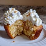 A hot chocolate cupcake cut in half showing the fluffy interior, white frosting, and toasted mini marshmallows.
