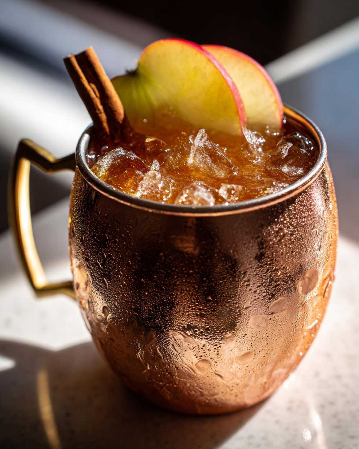 Close-up of a frosty copper mug filled with an apple cider moscow mule, garnished with apple slices and a cinnamon stick.