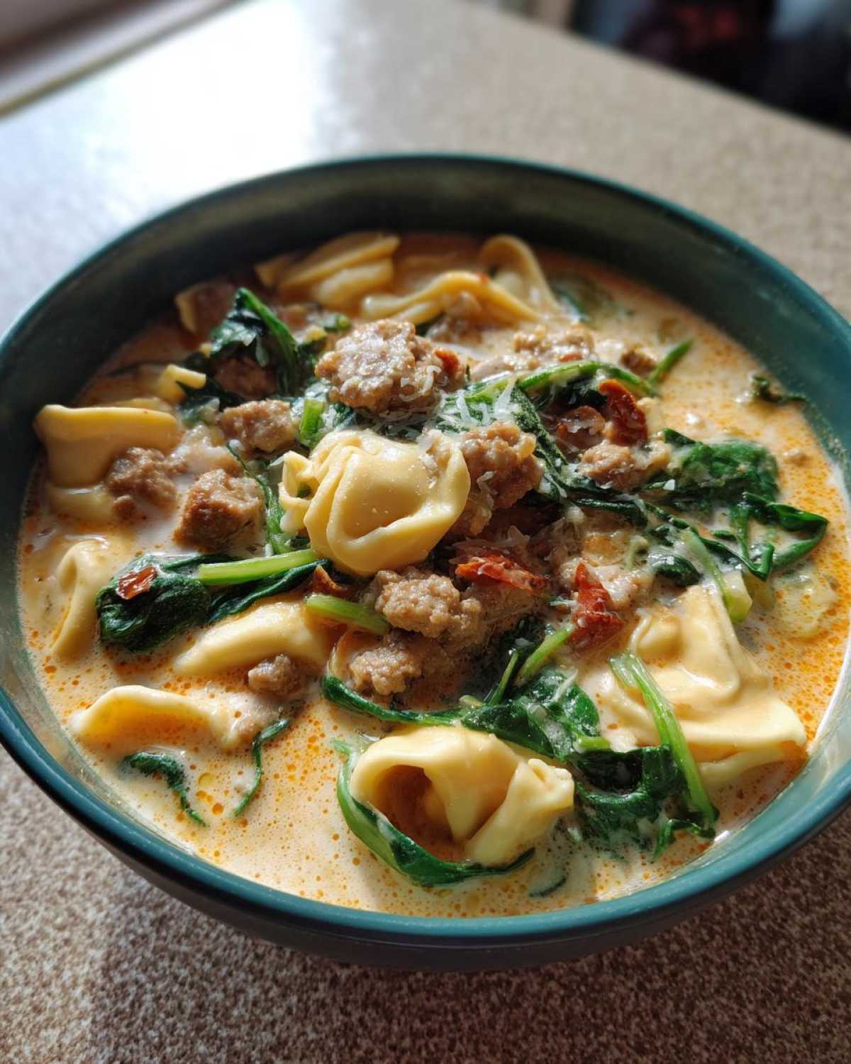 Close-up of a rich, creamy italian sausage tortellini soup with spinach and grated cheese.