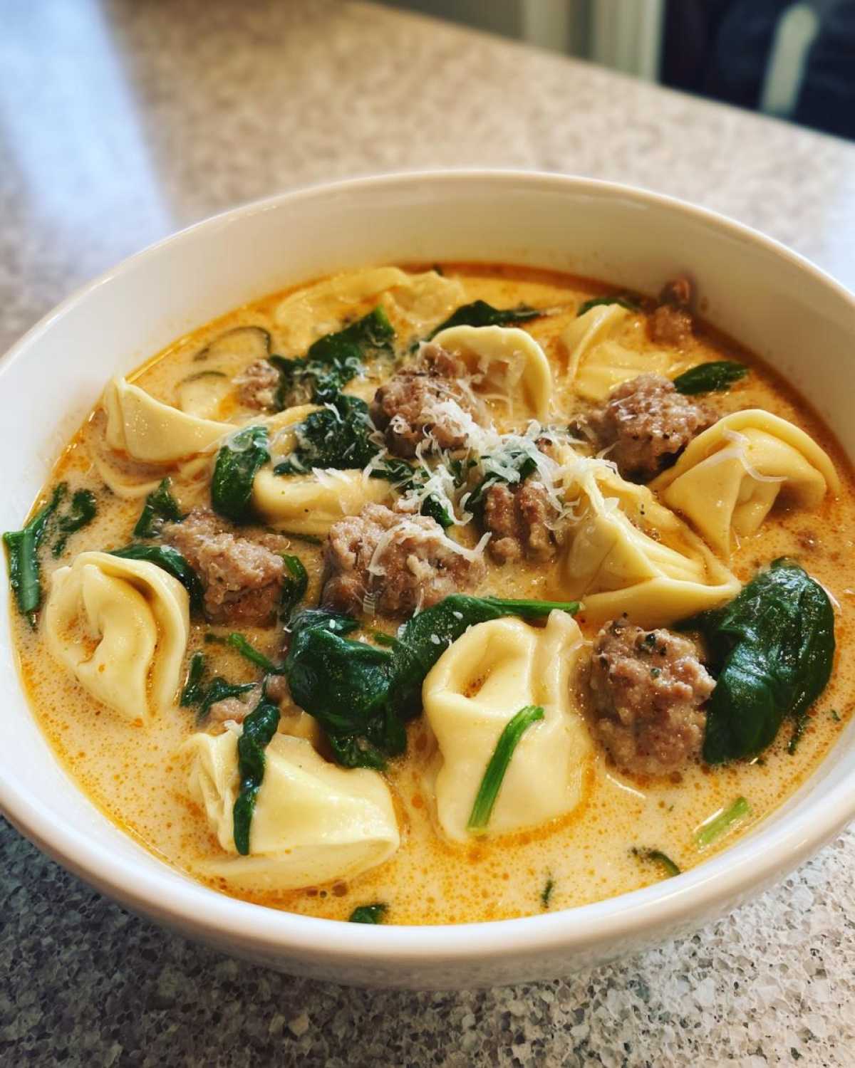 Close-up of a bowl of creamy italian sausage tortellini soup with spinach and grated Parmesan cheese.