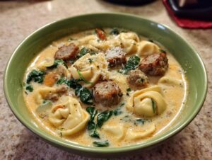Close-up of a bowl of creamy italian sausage tortellini soup topped with sausage chunks and Parmesan cheese.