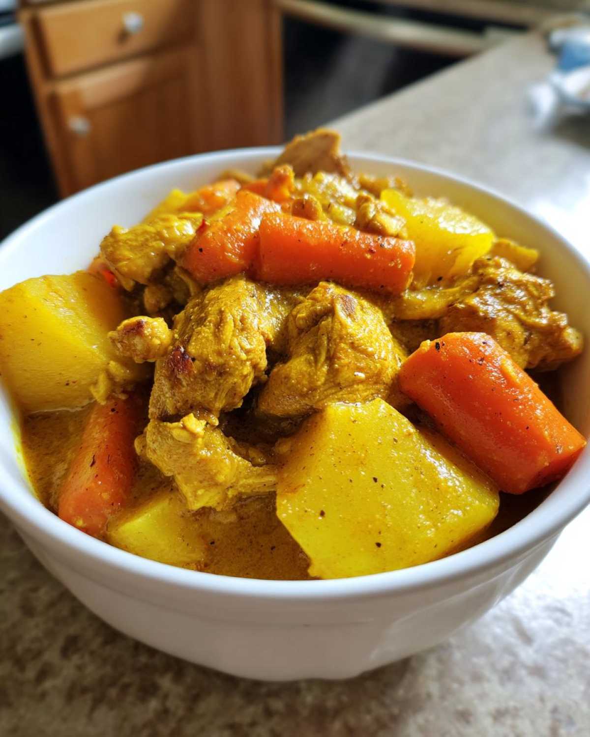 Close-up of chunks of chicken, potatoes, and carrots simmering in a rich, yellow sauce of Jamaican Curry Chicken.