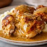 Close-up of crispy skin chicken and gravy generously poured over mashed potatoes, featuring a piece cut open.