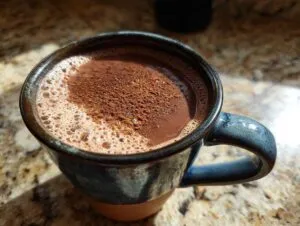 Close-up of a rich Mexican hot chocolate topped with cinnamon foam and powder in a rustic blue mug.