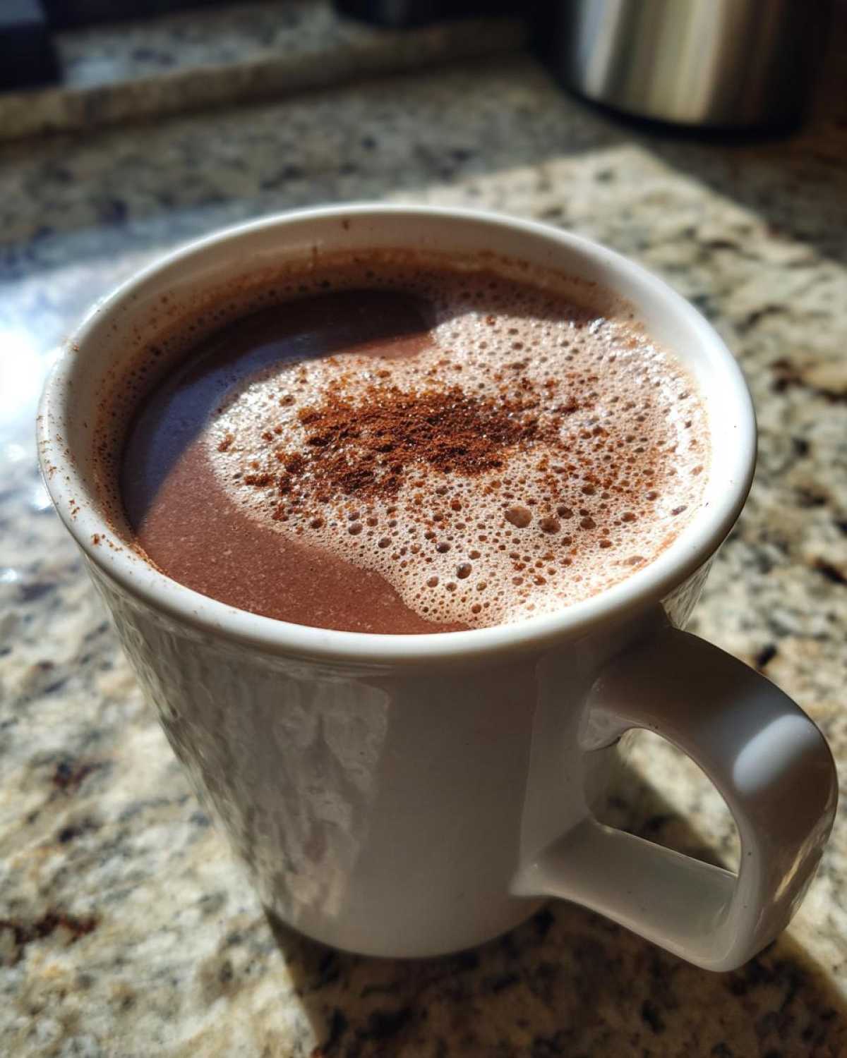 Close-up of a mug filled with foamy Mexican hot chocolate, dusted with cinnamon powder.
