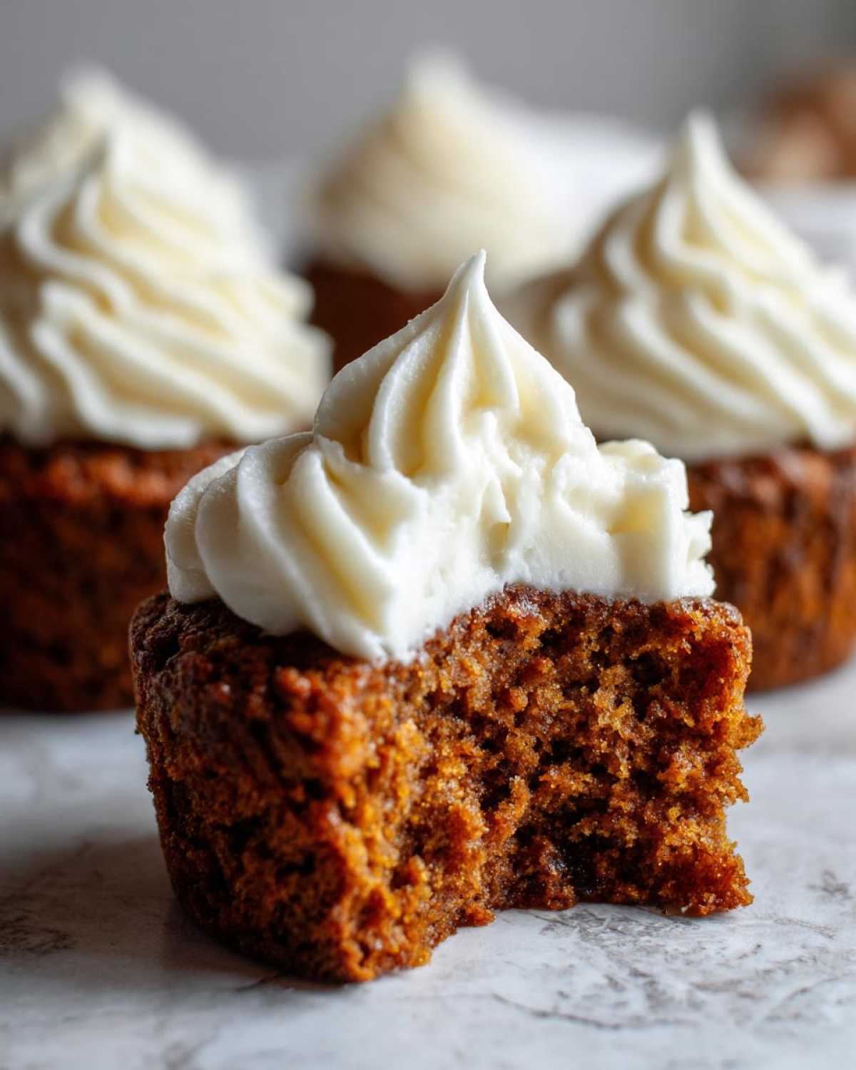 Close-up of a gingerbread cupcake with a bite taken out, showing the moist interior and thick cream cheese frosting.