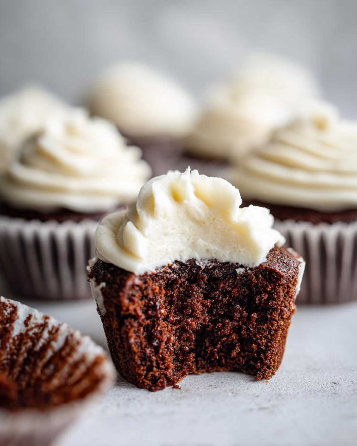 Close-up of a gingerbread cupcake with a bite taken out, showing the moist dark crumb and white frosting.