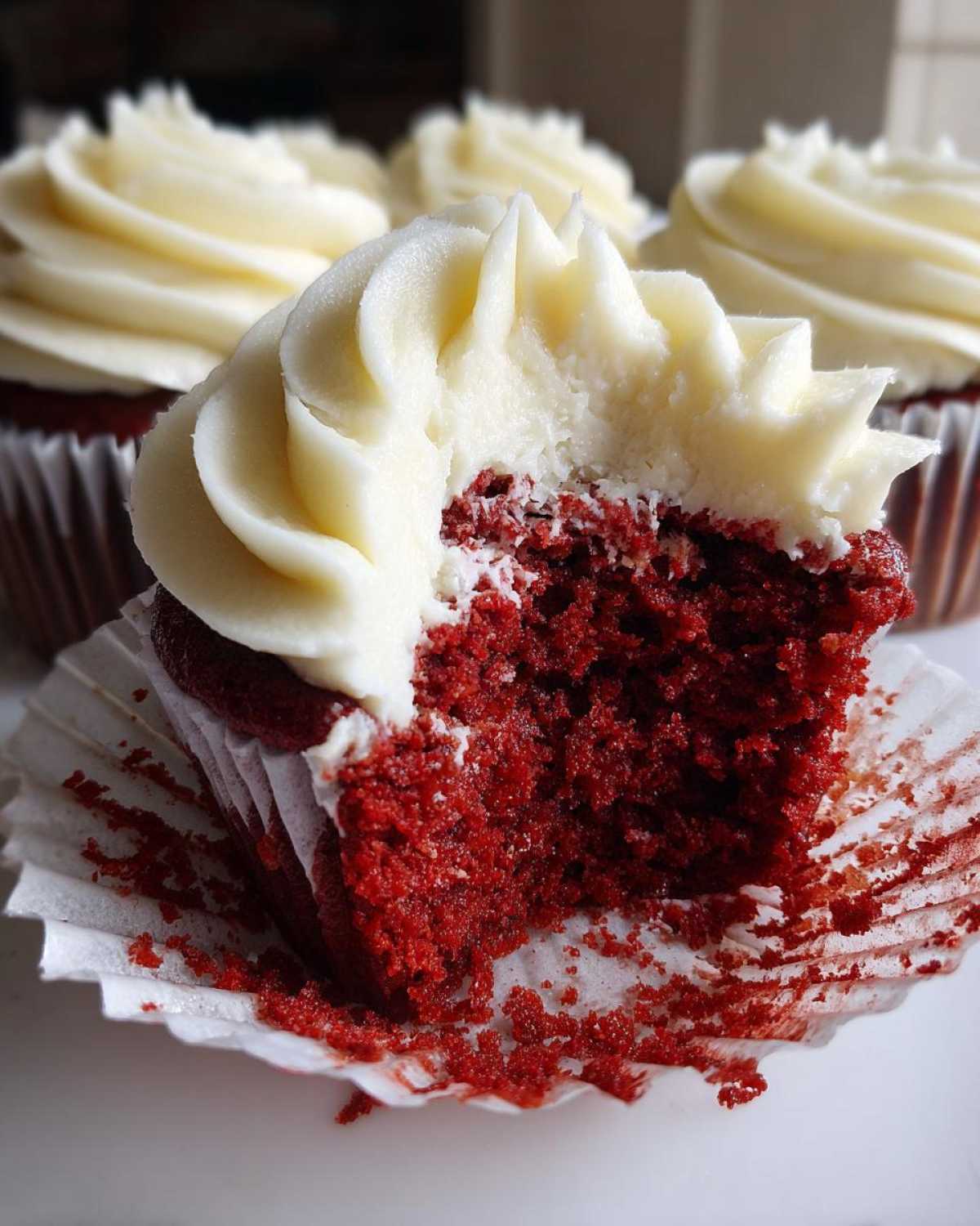 Close-up of a red velvet cupcake with a bite taken out, showing the moist red crumb and thick cream cheese frosting.