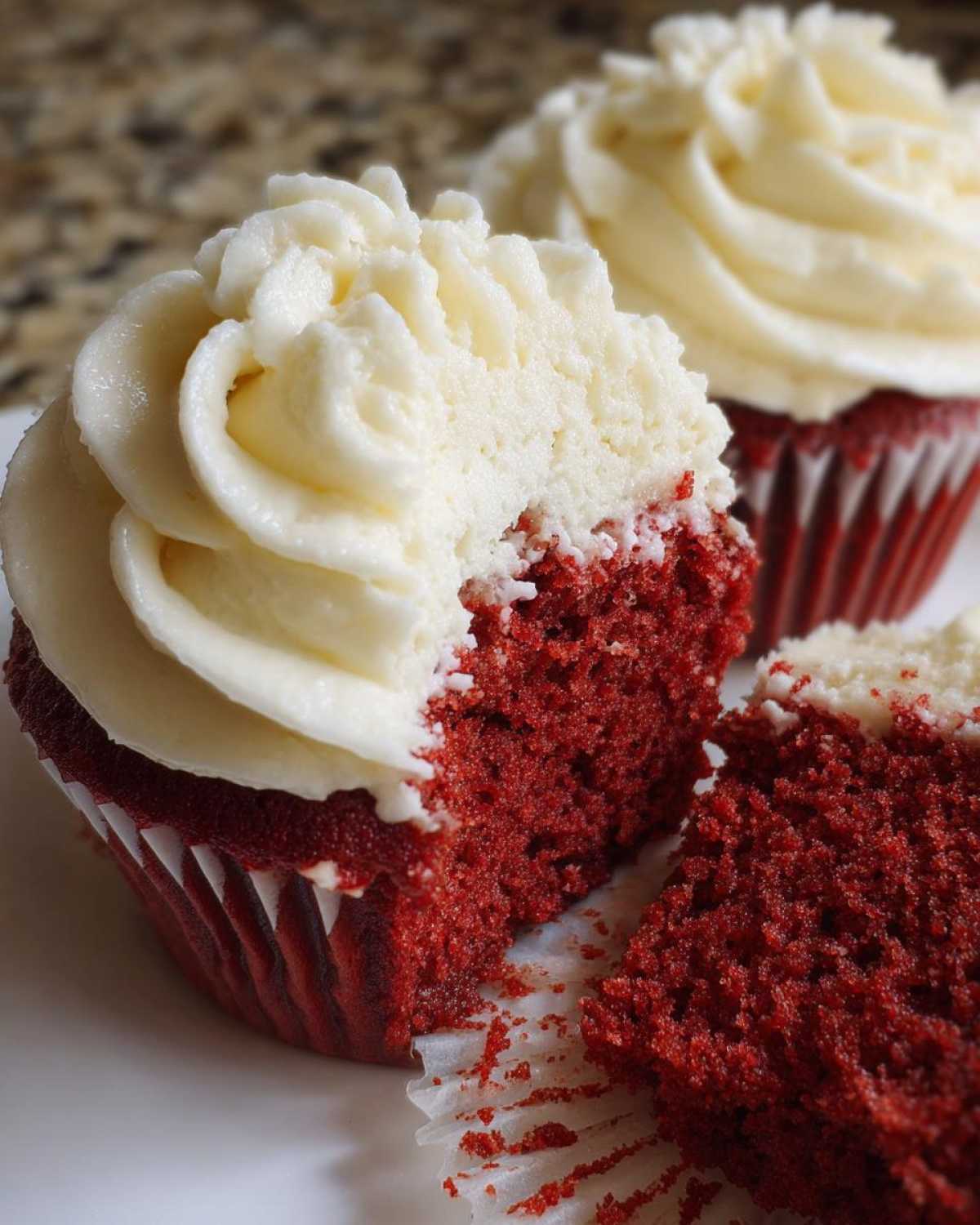 Close-up of a moist red velvet cupcake cut in half, showing the deep red crumb and thick cream cheese frosting.