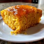 Close-up of a moist, golden slice of sweet potato cornbread topped with a shiny honey or maple glaze.