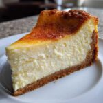 A thick, creamy slice of new york cheesecake with a graham cracker crust and a beautifully browned, slightly caramelized top.