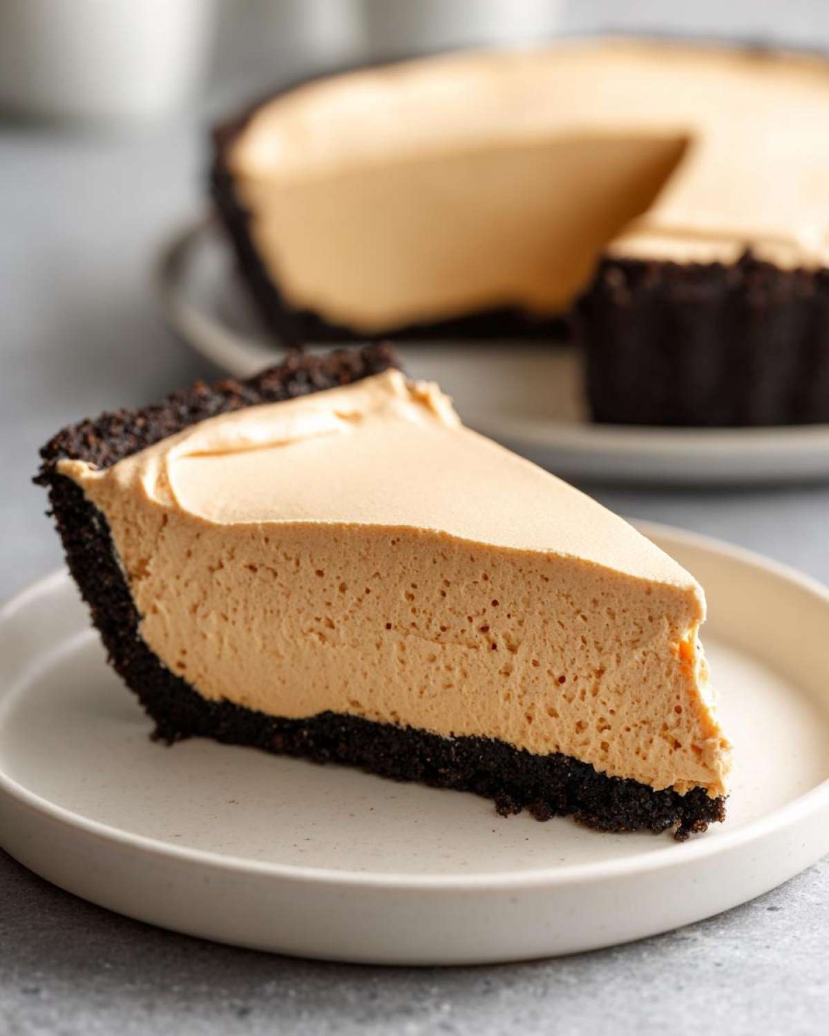 A close-up slice of no bake peanut butter pie featuring a thick, creamy peanut butter filling and a dark chocolate cookie crust.