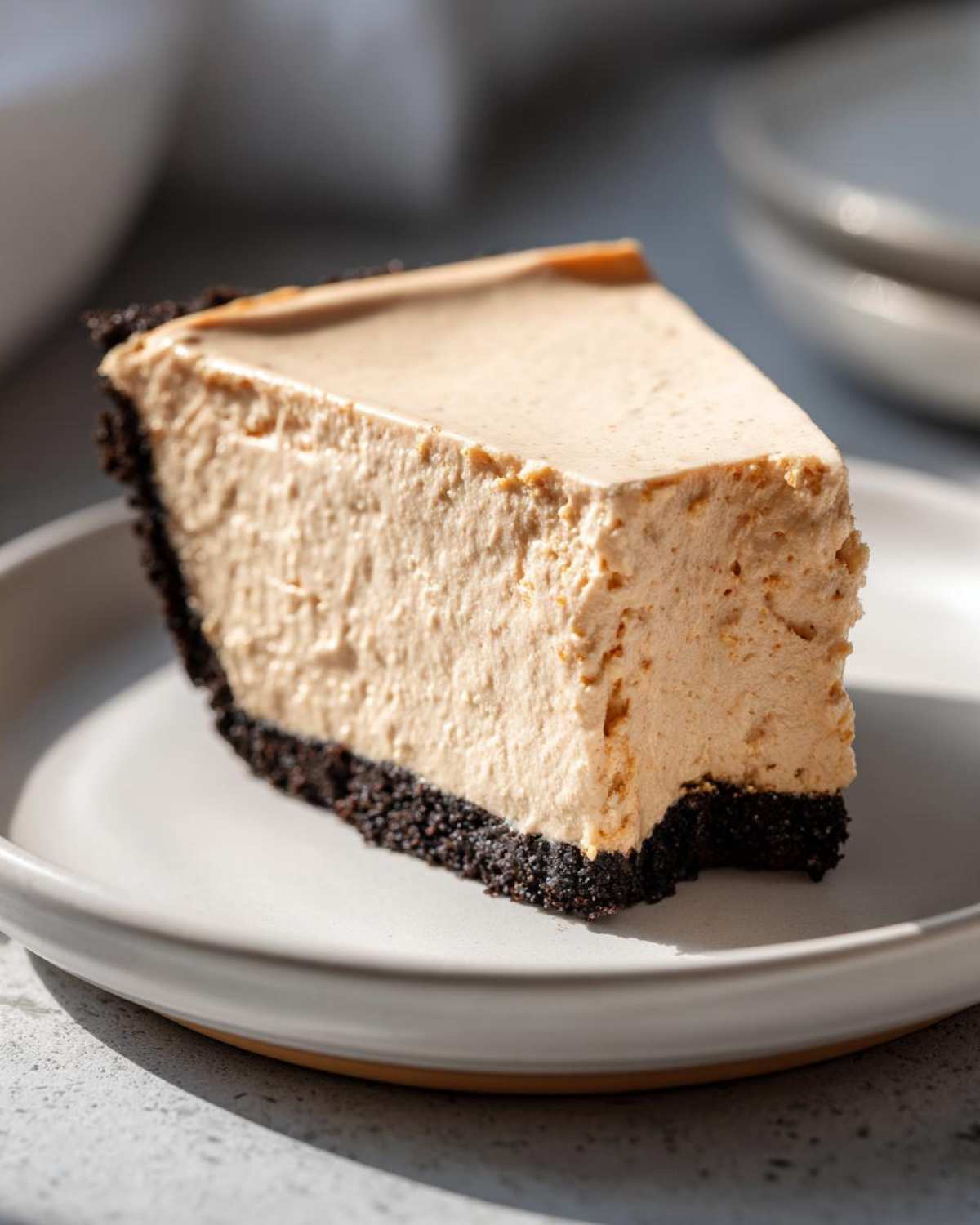 A close-up of a thick slice of no bake peanut butter pie featuring a creamy filling and dark chocolate crust on a light plate.