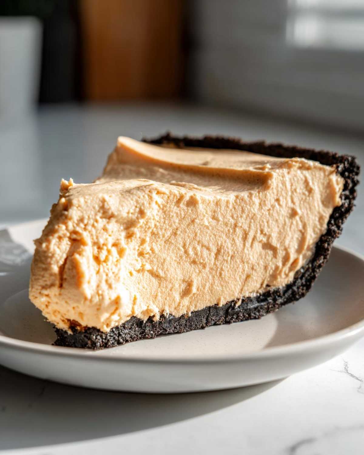 A thick slice of creamy no bake peanut butter pie featuring a rich, light brown filling and a dark chocolate cookie crust.