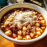 Close-up of a steaming bowl of pasta e fagioli topped generously with shredded Parmesan cheese.