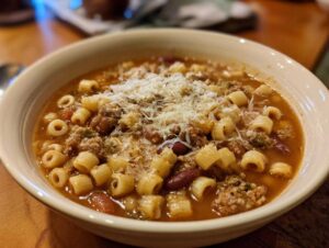 Close-up of a warm bowl of pasta e fagioli soup topped generously with grated Parmesan cheese.