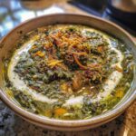 Close-up of a hearty bowl of Persian noodle soup topped with herbs and fried onions.