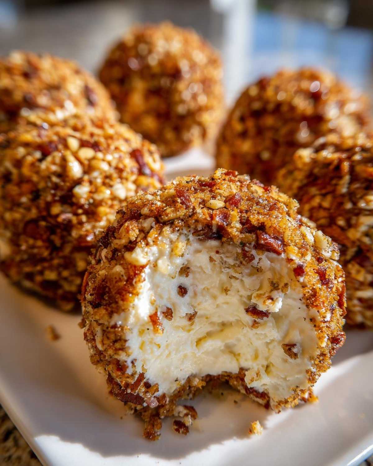 Close-up of a creamy pineapple cheese ball coated in nuts, with a bite taken out revealing the soft interior.