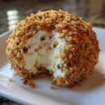 Close-up of a creamy pineapple cheese ball coated in chopped nuts, with a bite taken out.