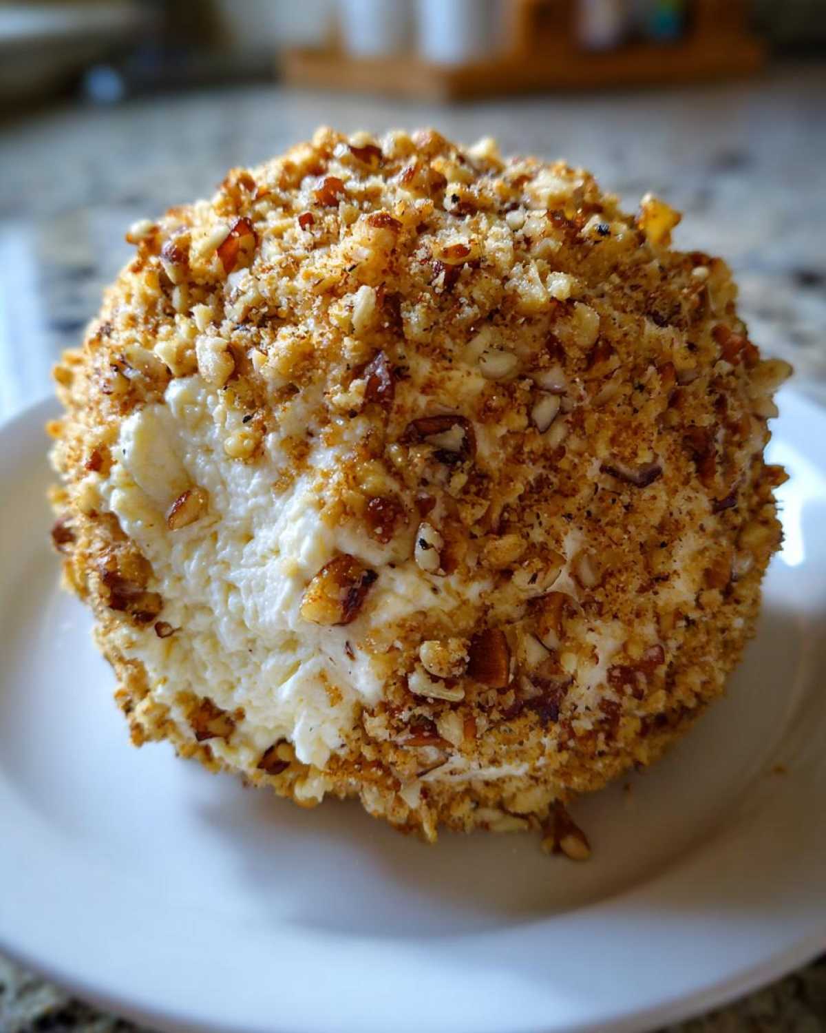 A close-up view of a creamy pineapple cheese ball coated entirely in chopped, toasted nuts.