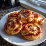A plate of five golden brown, cheesy pizza pinwheels dusted with herbs, ready to eat.
