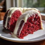 A close-up of a moist slice of red velvet bundt cake topped with thick white cream cheese glaze.