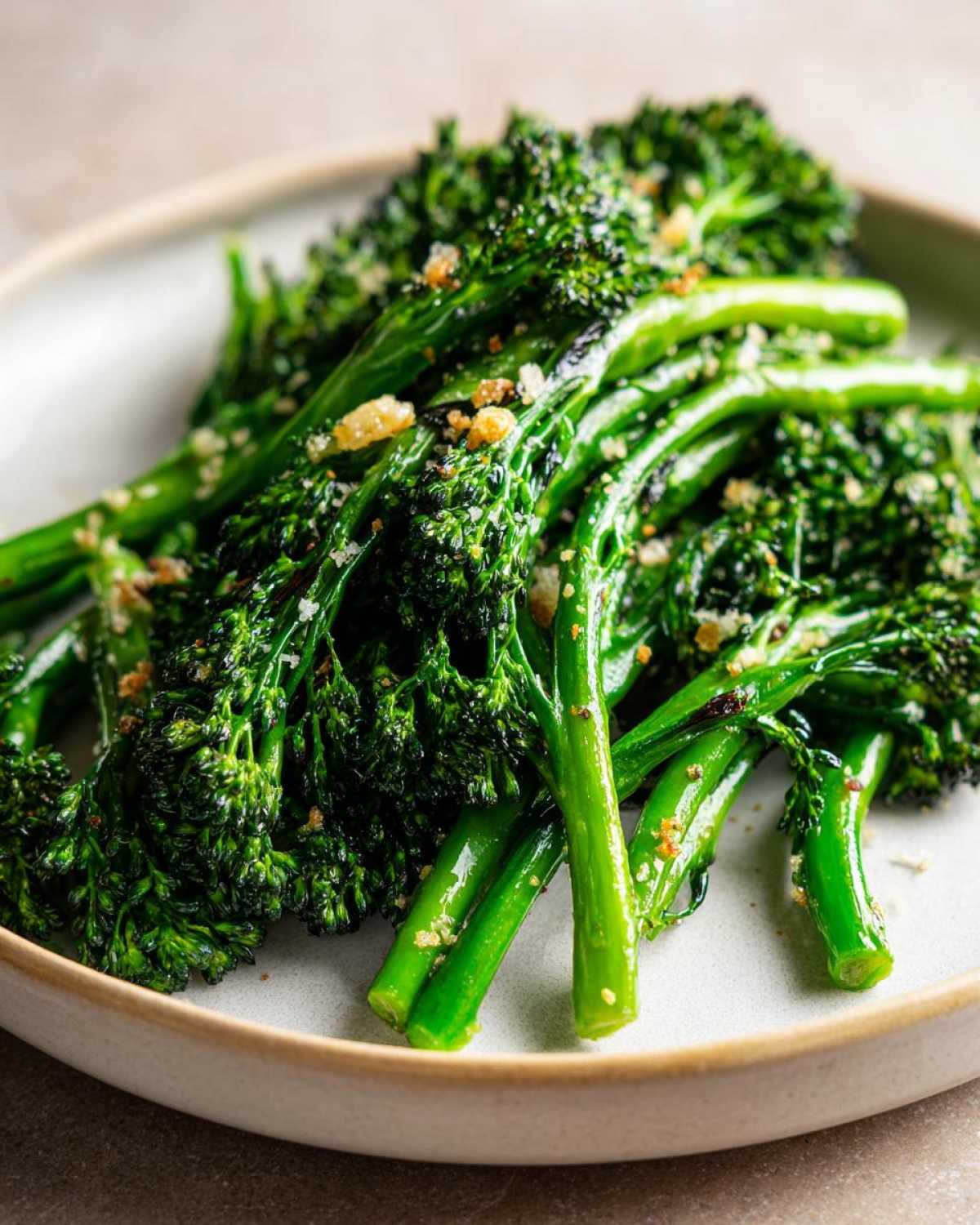 Close-up of bright green, roasted broccolini stalks topped with toasted breadcrumbs and seasoning.