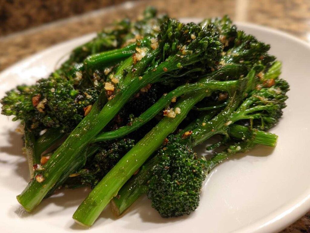 Close-up of bright green, roasted broccolini stalks seasoned with visible garlic bits on a white plate.