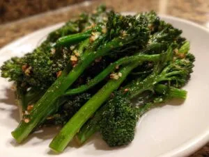 Close-up of bright green, roasted broccolini stalks seasoned with visible garlic bits on a white plate.
