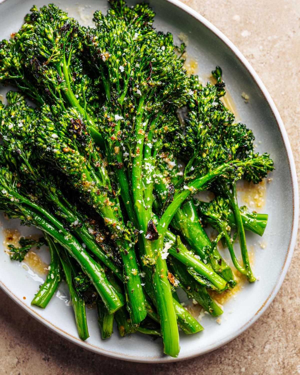 Close-up of vibrant green roasted broccolini seasoned with garlic and grated cheese on a light gray plate.