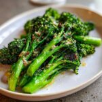 Close-up of bright green, glossy roasted broccolini topped with grated cheese and seasoning.