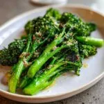 Close-up of bright green, glossy roasted broccolini topped with grated cheese and seasoning.