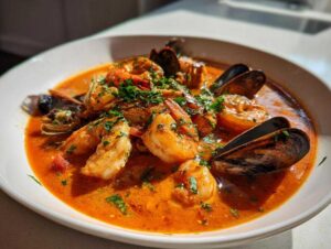 A close-up of a vibrant, rich seafood soup Cioppino featuring large shrimp and mussels in a tomato broth.