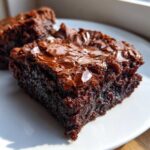 A close-up, mouthwatering shot of a fudgy square of brownies showing its signature shiny, crackled top.