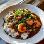 A bowl of rich, dark shrimp etouffee served over fluffy white rice and topped with chopped green onions.