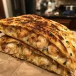 Close-up of a perfectly grilled shrimp quesadilla cut in half, showing melted cheese and seasoned shrimp filling.