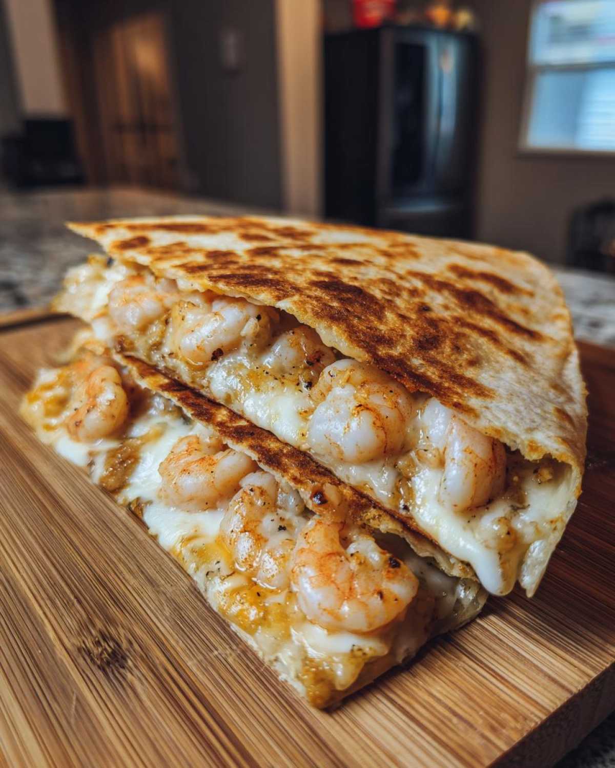 A close-up view of a perfectly grilled shrimp quesadilla slice overflowing with melted cheese and seasoned shrimp.
