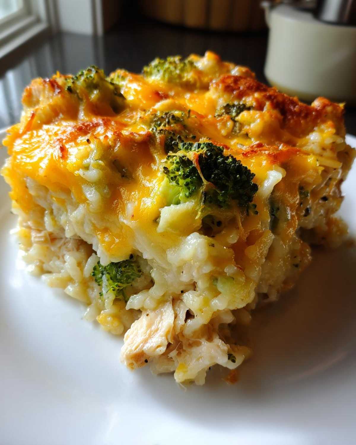 A close-up slice of creamy chicken broccoli rice casserole topped with melted, browned cheddar cheese.