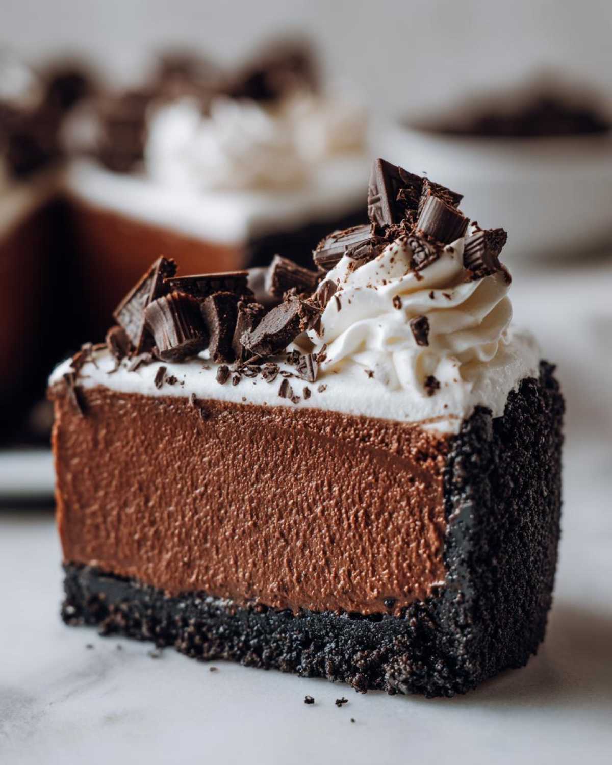 Close-up of a decadent slice of chocolate mousse pie with a dark crust, topped with whipped cream and chocolate shavings.