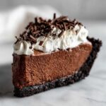 A decadent slice of chocolate mousse pie with a dark crust, topped with whipped cream and chocolate shavings.