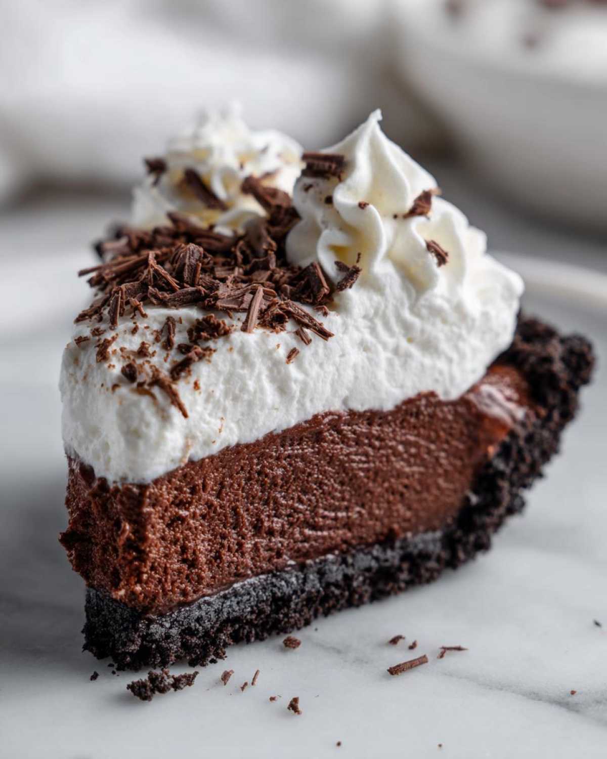 A decadent slice of chocolate mousse pie featuring a dark crust, thick chocolate filling, and topped with whipped cream and chocolate shavings.