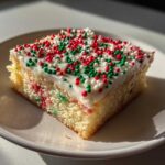 A square slice of christmas sugar cookie bars topped with white frosting and red, green, and white sprinkles.