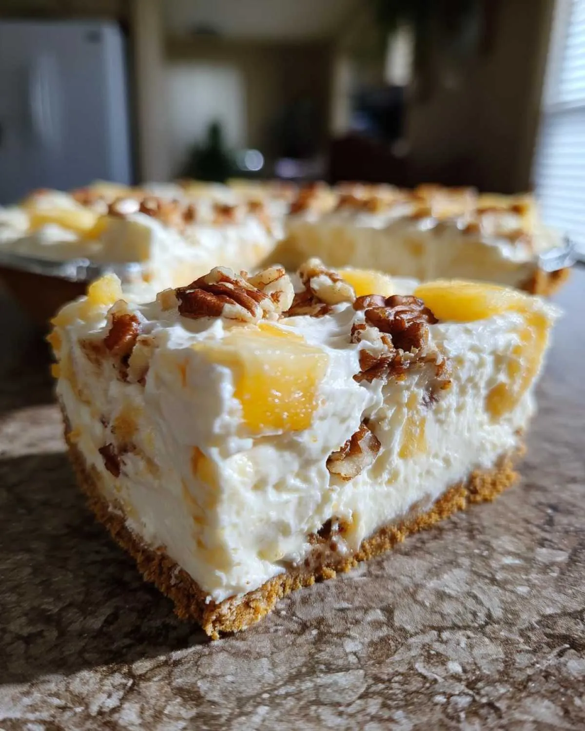 Close-up of a slice of creamy millionaire pie showing the graham cracker crust, pineapple chunks, and pecan topping.
