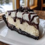 A generous slice of creamy ice cream pie with a dark cookie crust, topped with whipped cream and chocolate syrup.